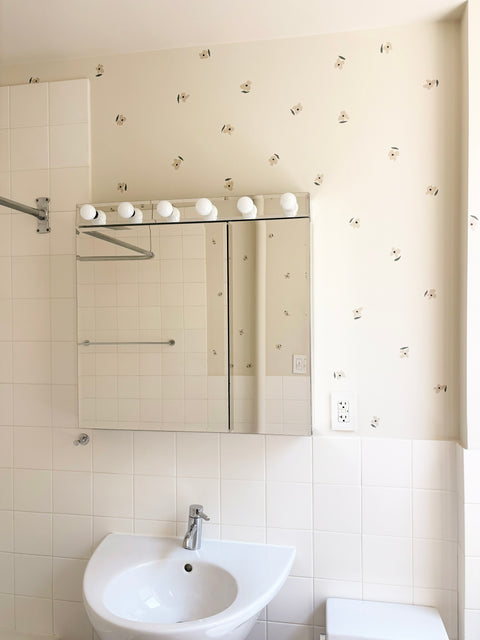 Cream bathroom wall with scattered small floral sticker decals above white subway tile and pedestal sink